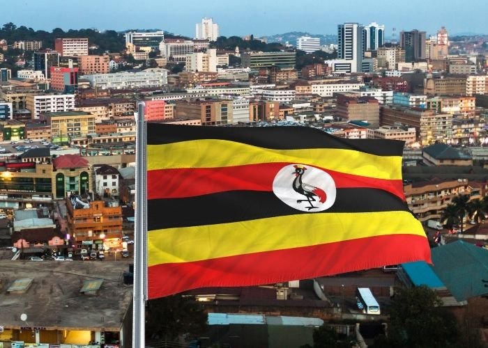 Pai agredido pelos filhos em Uganda após conversão ao cristianismo 1 Bandeira de Uganda tendo ao fundo a cidade de Kampala Foto Montagem FolhaGospelCanva Pro