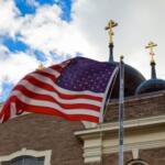 EUA encerram 2026 sem acolher refugiados perseguidos por religião, revela relatório 3 Bandeira dos EUA e duas cruzes no topo de uma igreja Foto Canva Pro