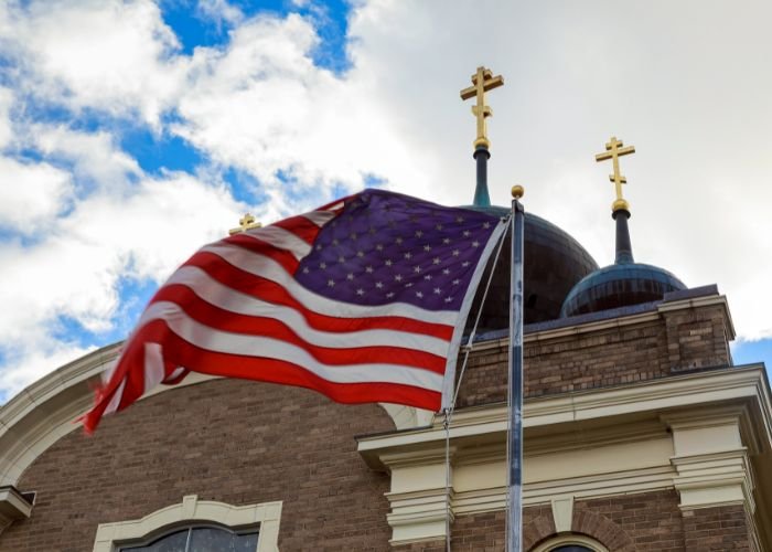 EUA encerram 2026 sem acolher refugiados perseguidos por religião, revela relatório 1 Bandeira dos EUA e duas cruzes no topo de uma igreja Foto Canva Pro