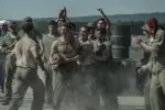 Peter Berg retrata sacrifício e amizade em filme sobre a Segunda Guerra na Netflix 4 "A group of WWII-era soldiers in dusty uniforms are shouting and cheering around two men, possibly during a brawl or contest, outdoors near metal barrels and mountains in the background."