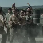 Peter Berg retrata sacrifício e amizade em filme sobre a Segunda Guerra na Netflix 3 "A group of WWII-era soldiers in dusty uniforms are shouting and cheering around two men, possibly during a brawl or contest, outdoors near metal barrels and mountains in the background."