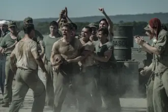 Peter Berg retrata sacrifício e amizade em filme sobre a Segunda Guerra na Netflix 5 "A group of WWII-era soldiers in dusty uniforms are shouting and cheering around two men, possibly during a brawl or contest, outdoors near metal barrels and mountains in the background."