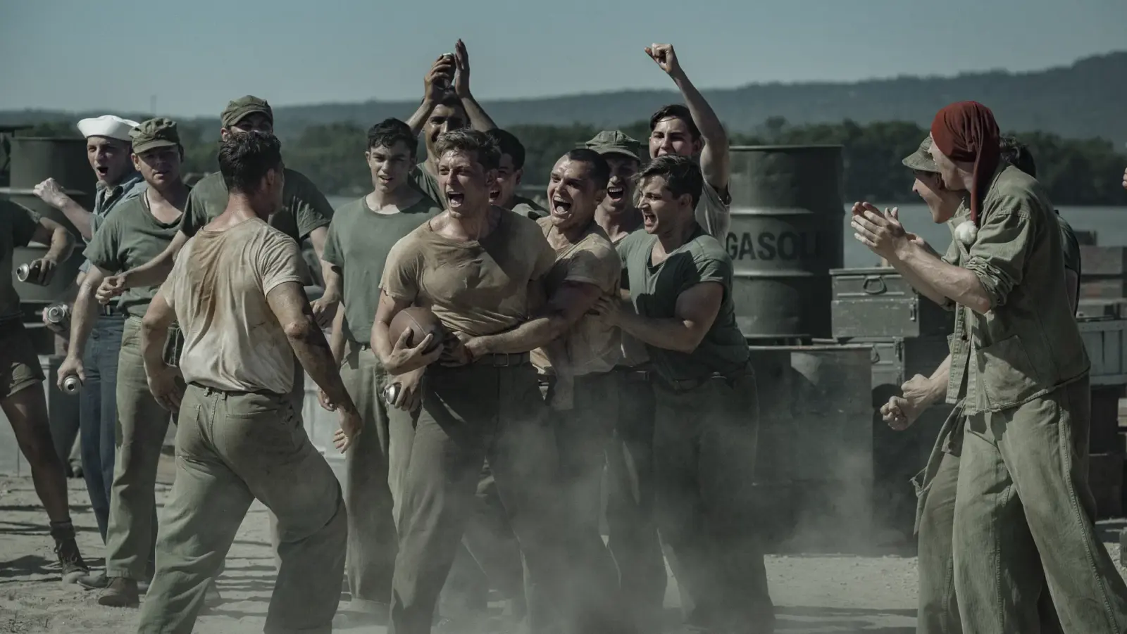 Peter Berg retrata sacrifício e amizade em filme sobre a Segunda Guerra na Netflix 1 "A group of WWII-era soldiers in dusty uniforms are shouting and cheering around two men, possibly during a brawl or contest, outdoors near metal barrels and mountains in the background."